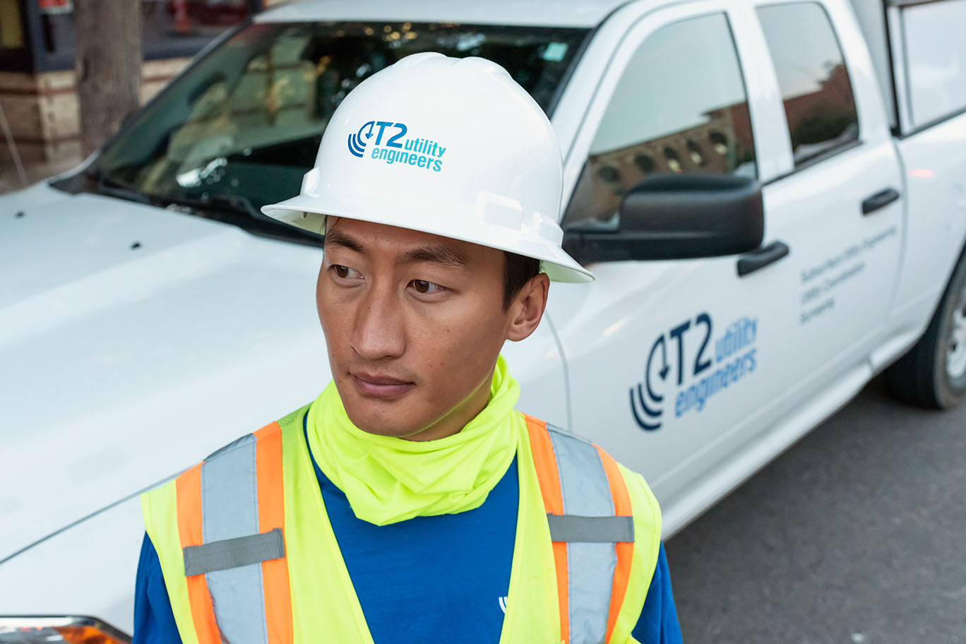 Commercial photographty Golden Colorado near Denver depicts a T2 Utility engineer with COVID mask ready. The image, created for an advertising project for the utilities firm features an Asian American engineer looking off camera with logos on his hardhat and on service vehicle behind him.